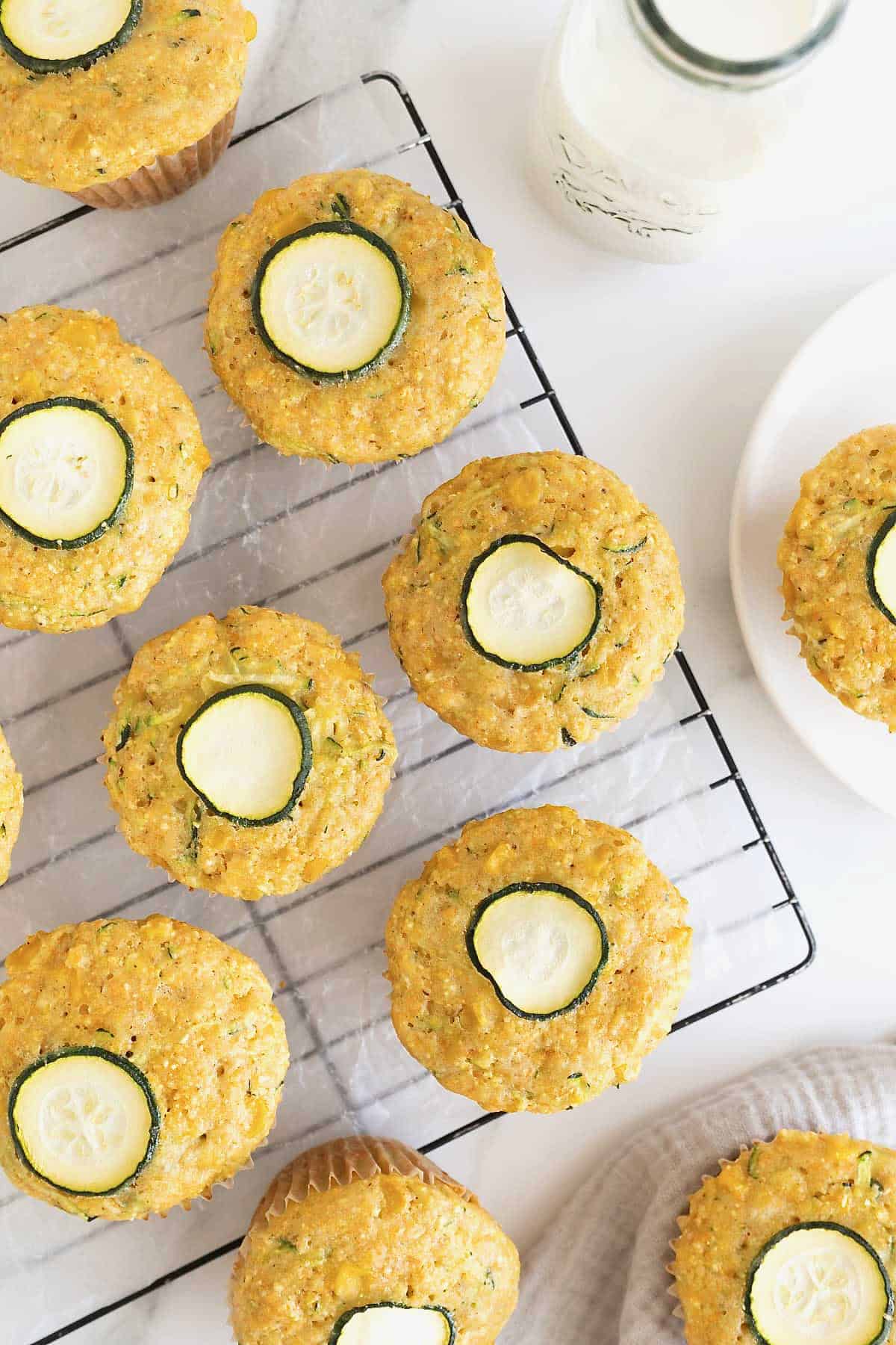 Corn muffins with a thin slice of zucchini on top. The muffins are sitting on a wire cooling rack.