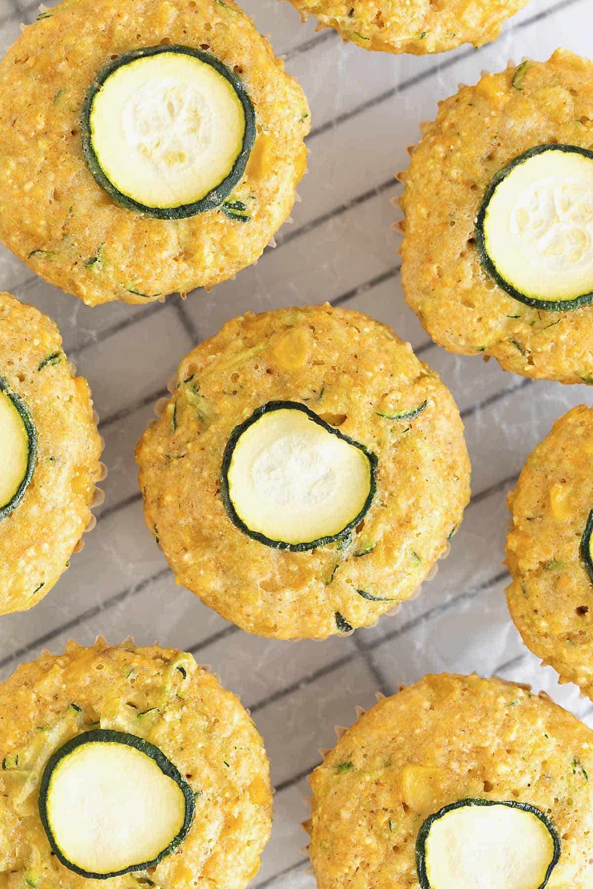 Corn muffins with a thin slice of zucchini on top. The muffins are sitting on a wire cooling rack.