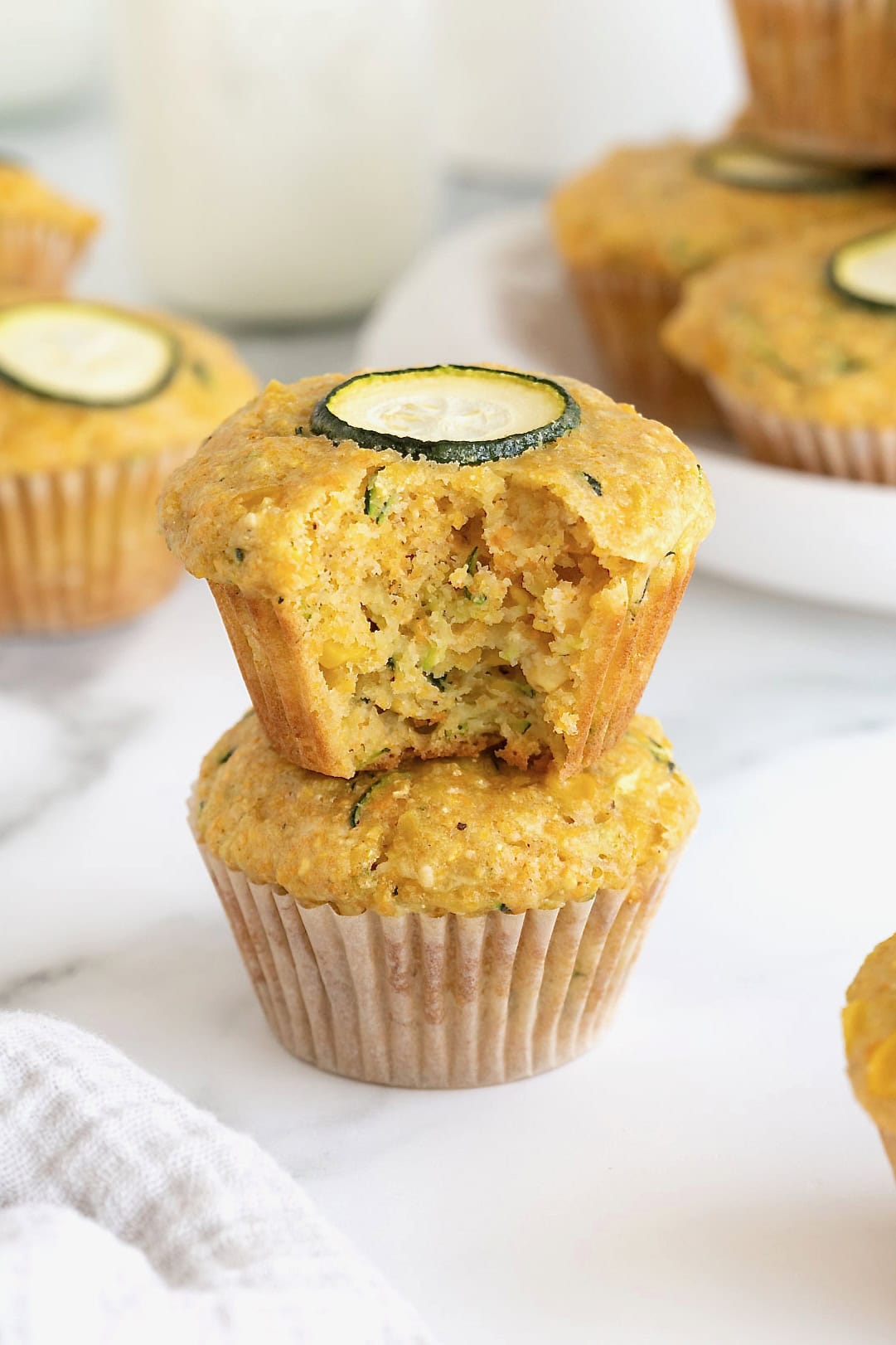 Two zucchini corn muffins stacked on a white marble counter.