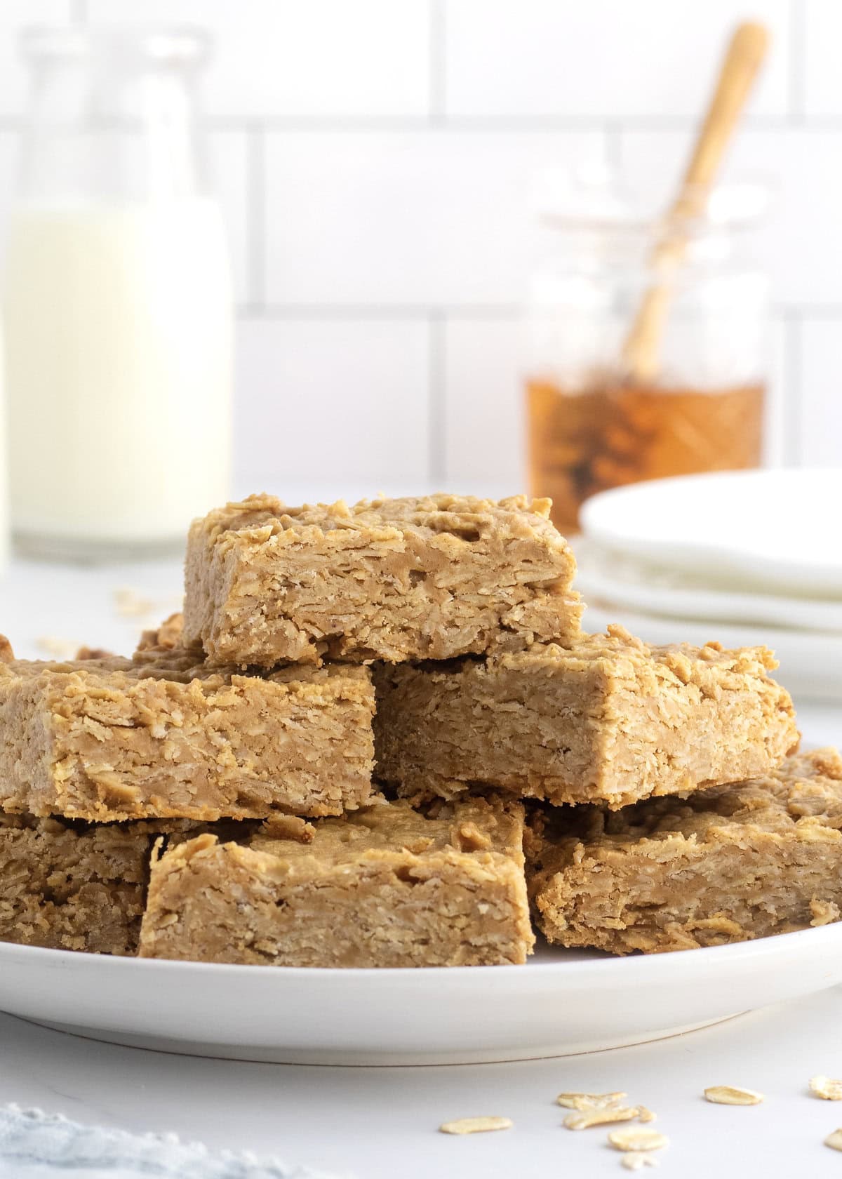 Six peanut butter honey oat bars piled on a rimmed white plate.