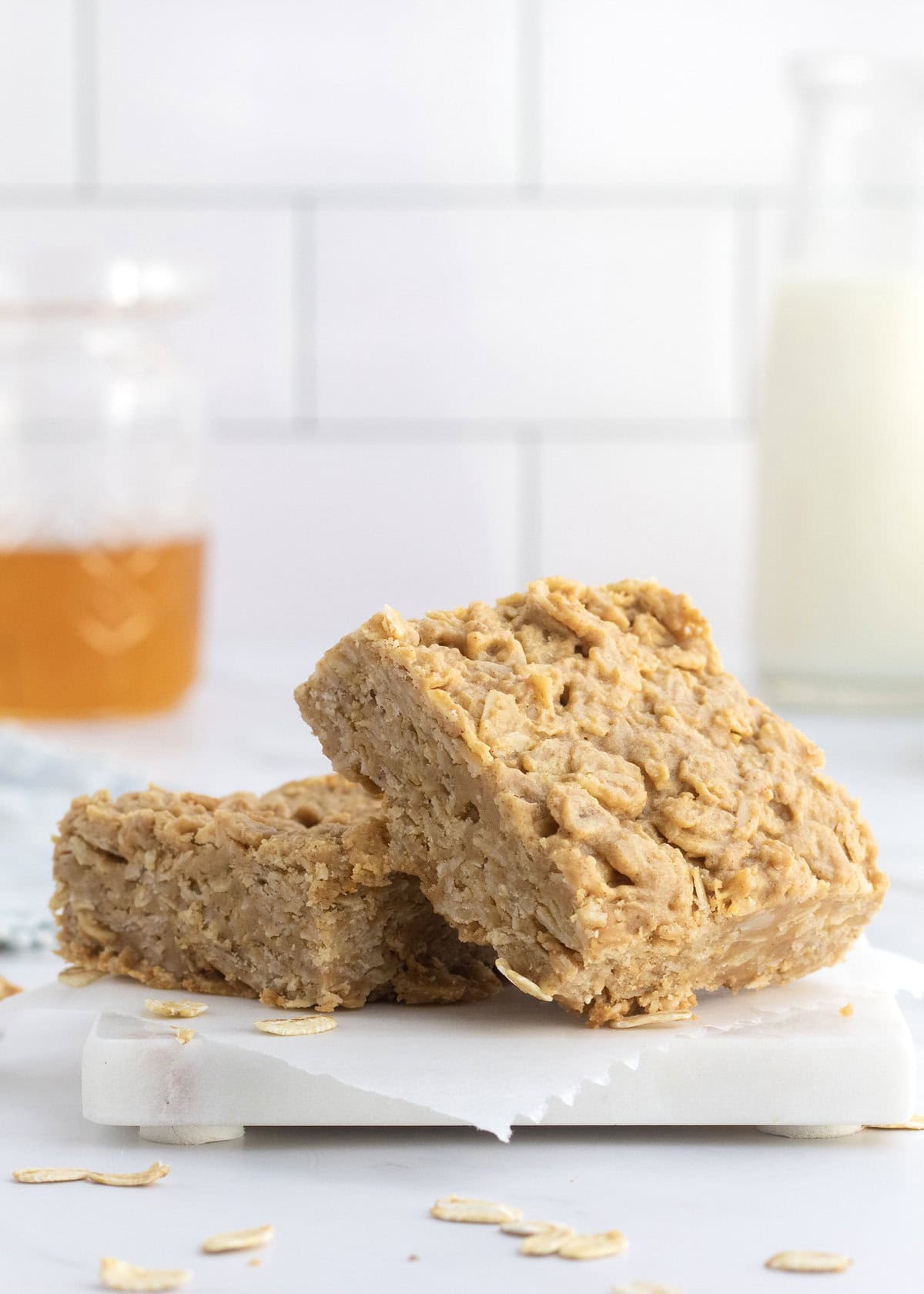 Two peanut butter honey oat bars on a white marble counter. There is a jar of honey in the upper left background.