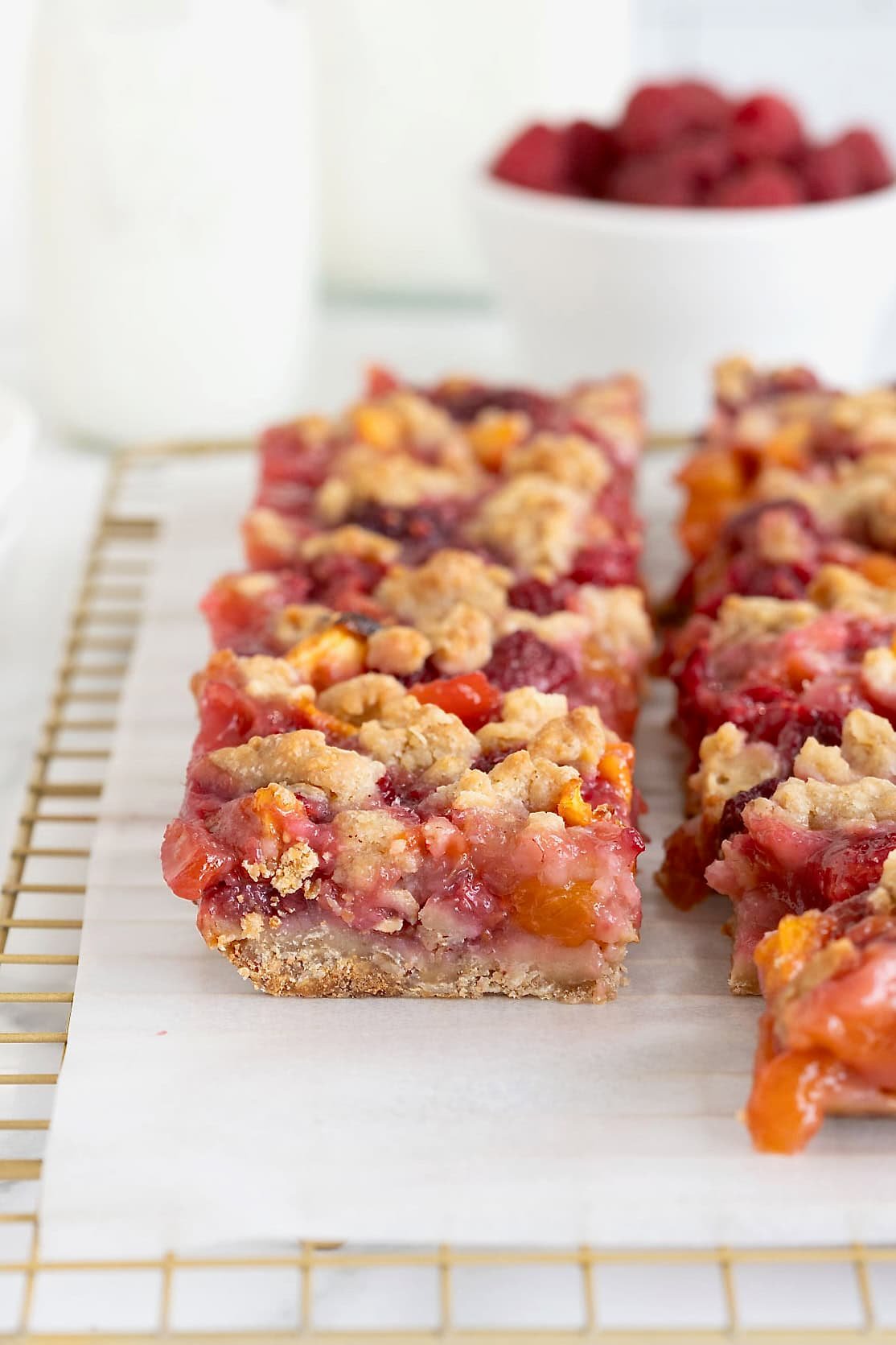 Peach raspberry crumb bars on a parchment lined gold-toned wire cooling rack.
