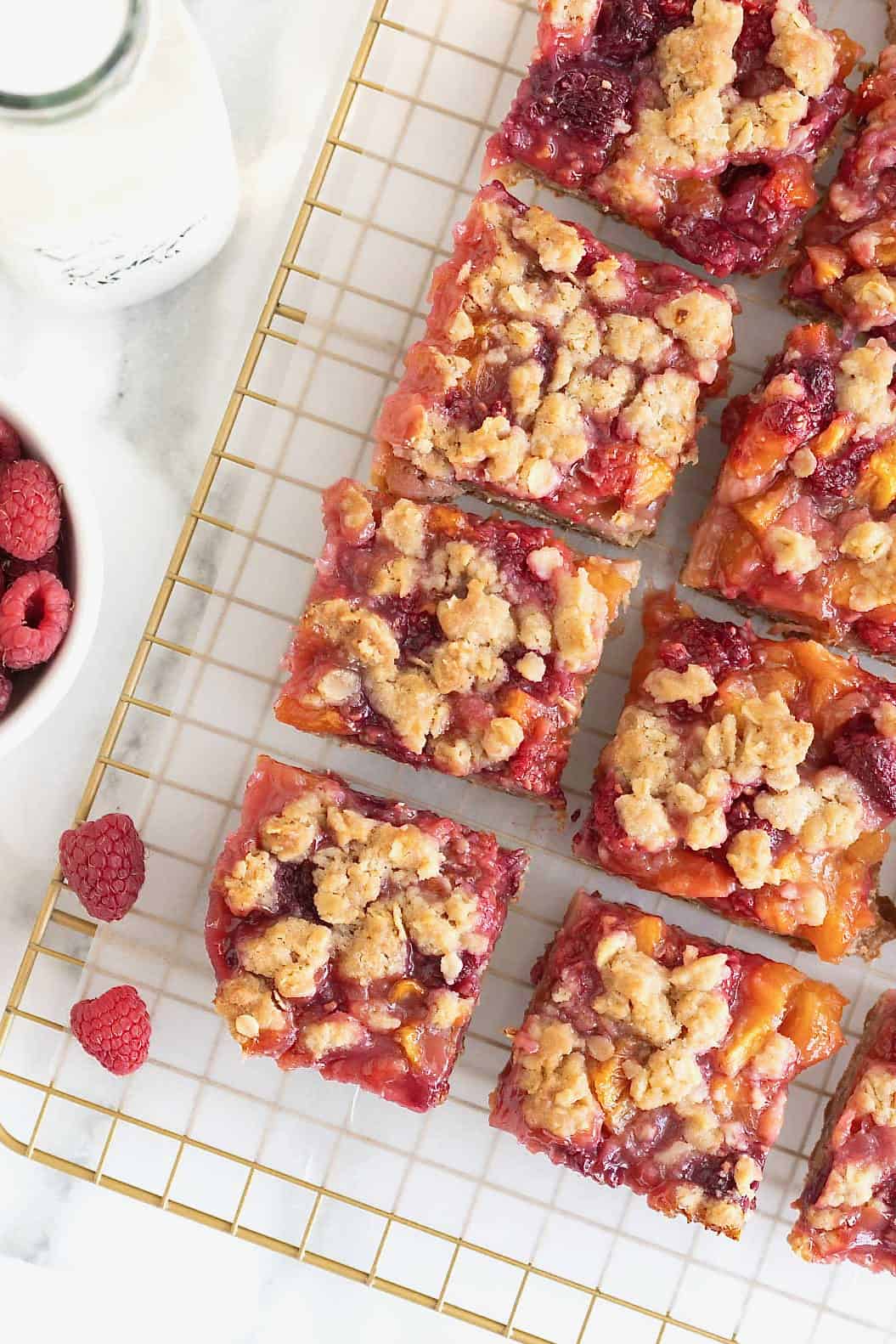 Peach raspberry crumb bars on a parchment lined gold-toned wire cooling rack.