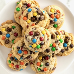 A white plate with a pile of cookies with M&Ms and chocolate chips in them.
