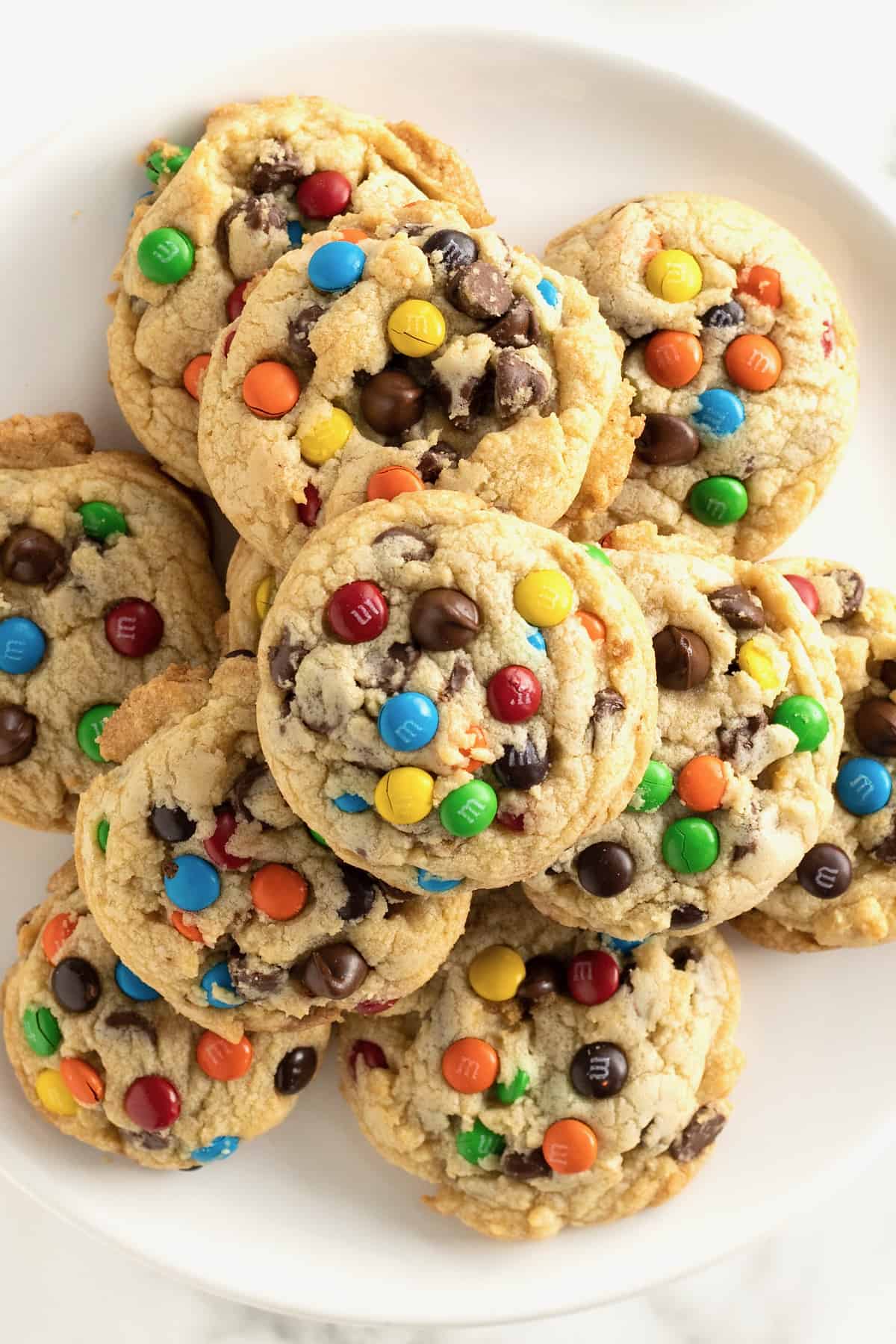 A white plate with a pile of cookies with M&Ms and chocolate chips in them.