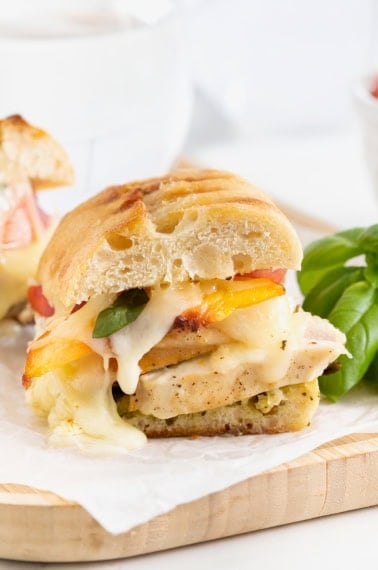 Chicken Pesto Peach Panini cut in half on a parchment lined light wood cutting board.