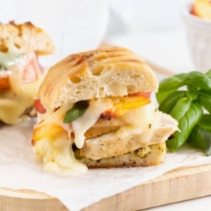 Chicken Pesto Peach Panini cut in half on a parchment lined light wood cutting board.