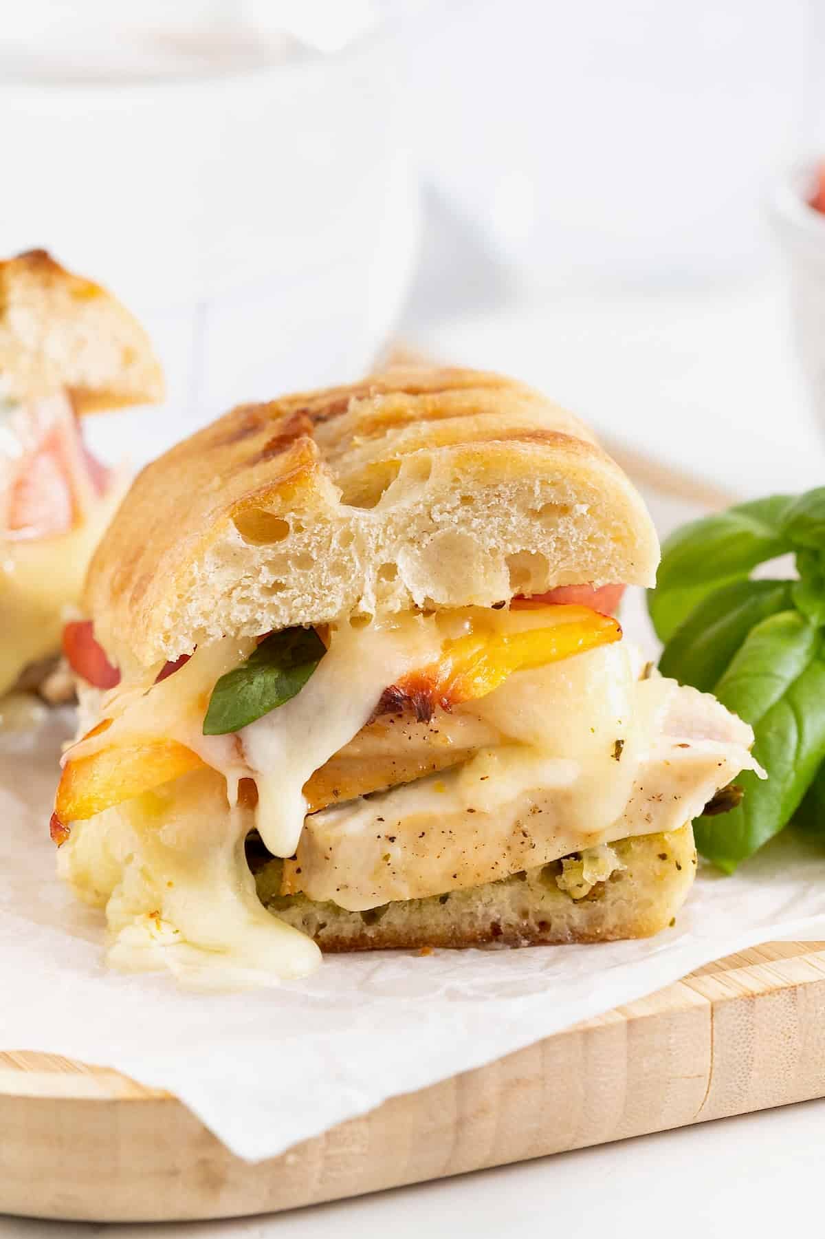 Chicken Pesto Peach Panini cut in half on a parchment lined light wood cutting board.