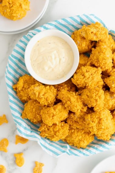 A plate of goldfish chicken nuggets next to a small white dish of ranch dressing.
