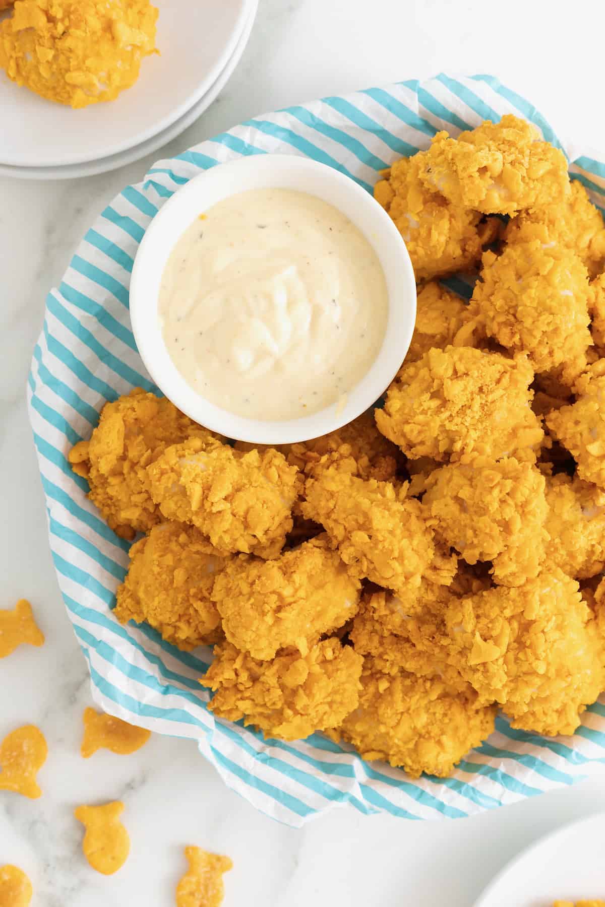A plate of goldfish chicken nuggets next to a small white dish of ranch dressing.