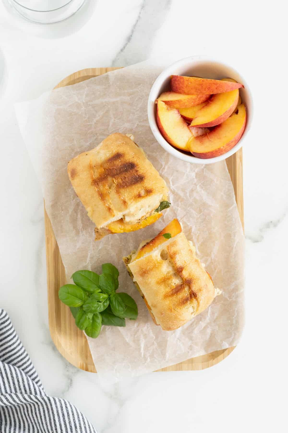 a grilled panini with chicken, peaches and pesto cut in half on a parchment lined wood cutting board.