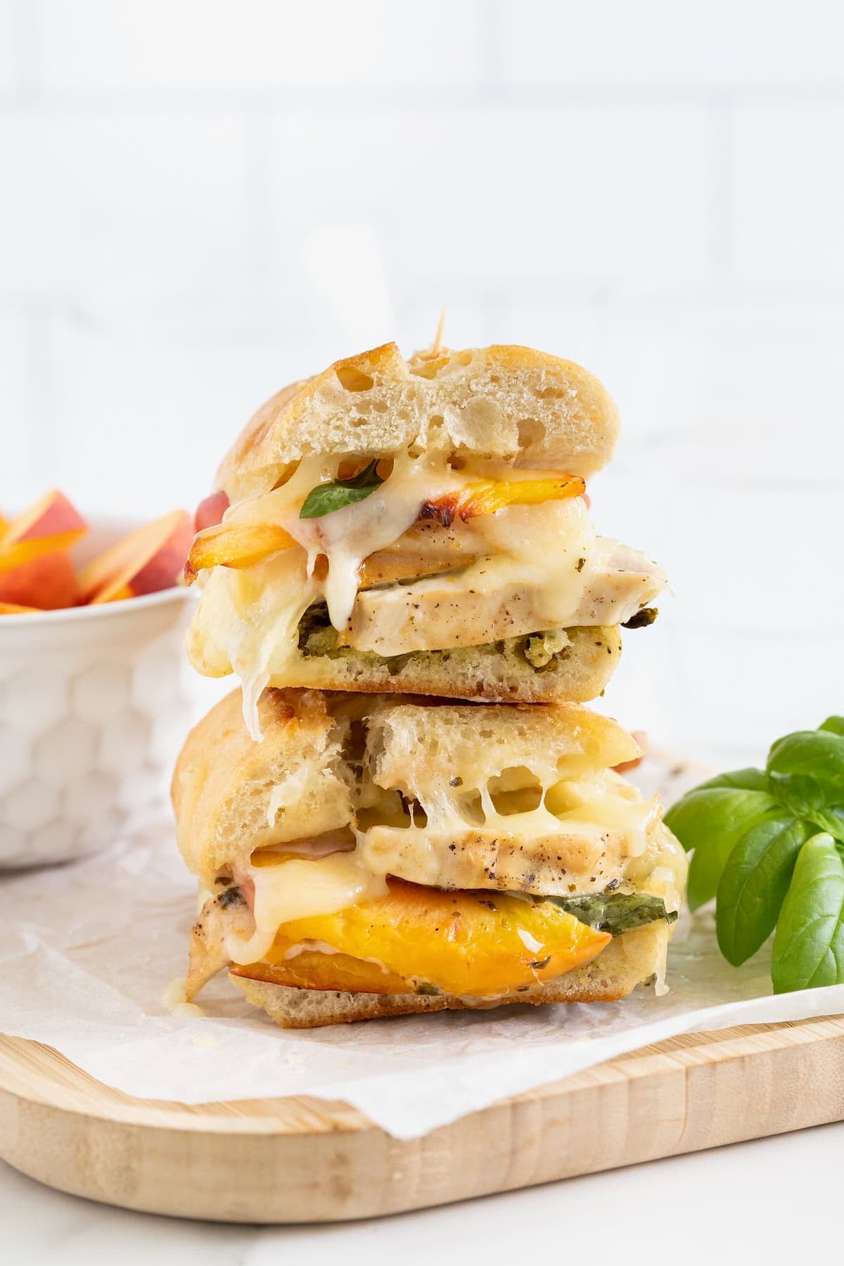 Two halves of a chicken pesto peach panini stacked on a parchment lined wood cutting board.