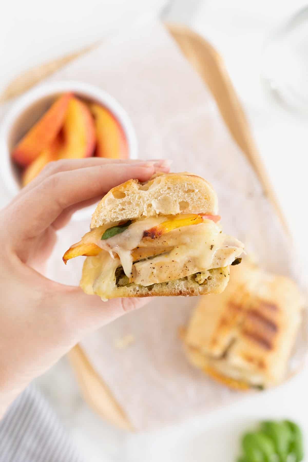 a hand holding a peach panini with chicken and pesto.