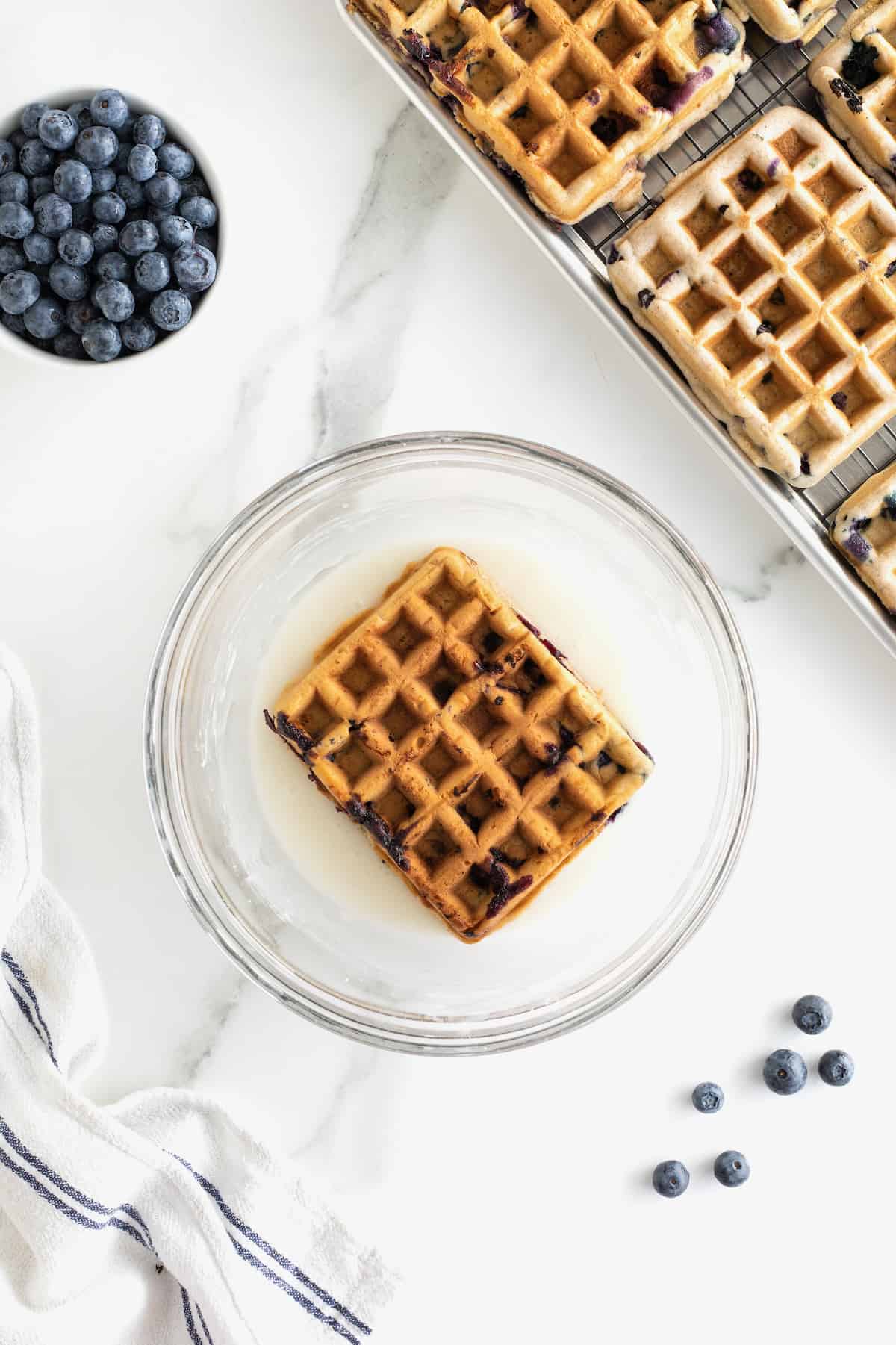 A blueberry waffle laying in a glass bowl of white glaze.