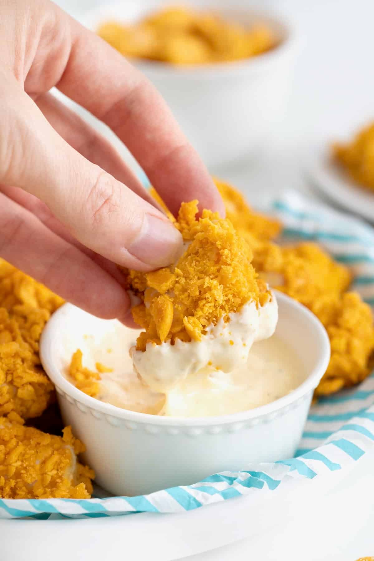 A hand dipping a goldfish chicken nugget into a small white dish of ranch dressing.