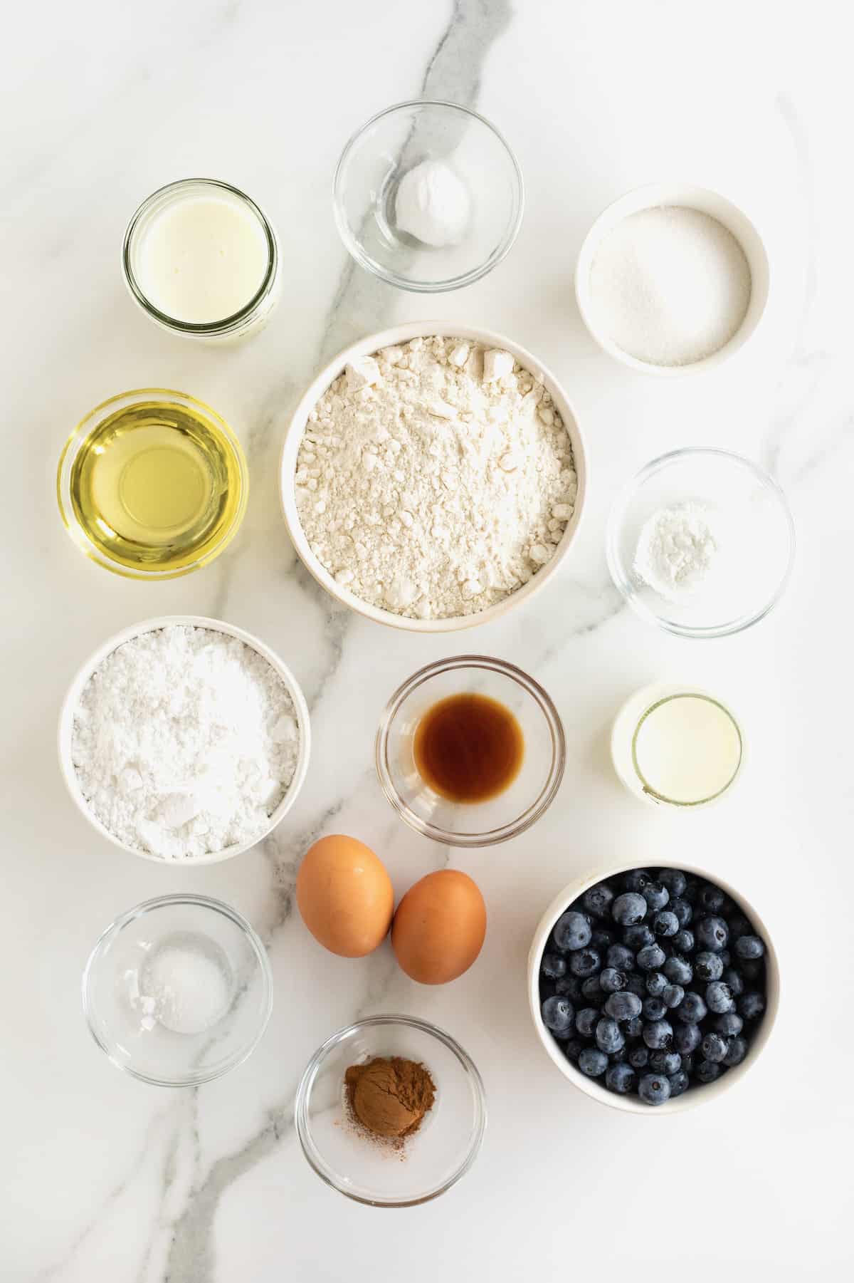 Ingredients used to make blueberry cake waffles in small glass dishes on a white marble counter