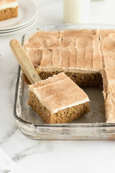 A zucchini sheet cake in a glass dish with cinnamon cream cheese frosting.