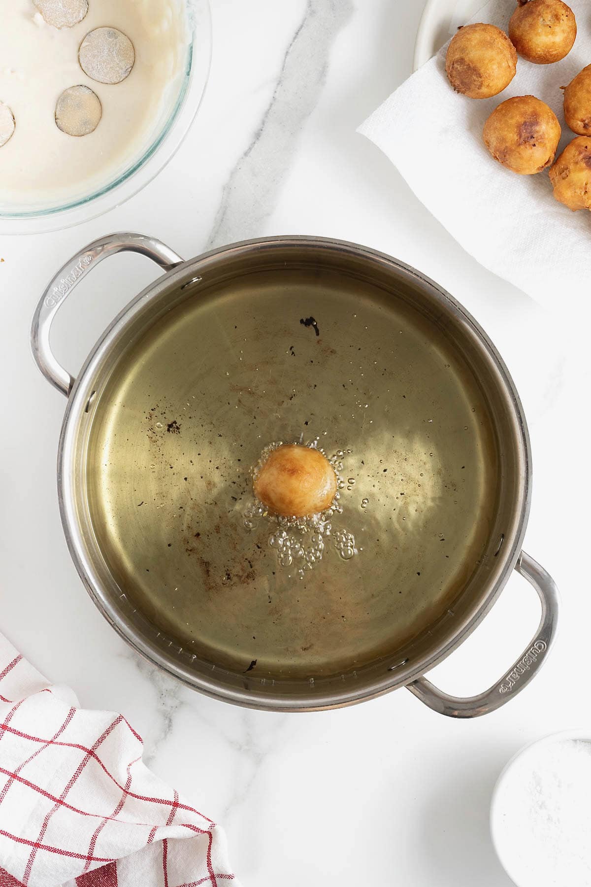 A large frying pan of oil with a single fried cookie dough ball in it.
