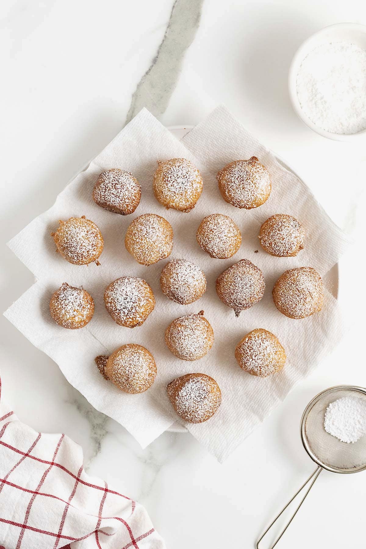 Powdered sugar dusted on fried cookie dough bites on a white plate lined with paper towels.