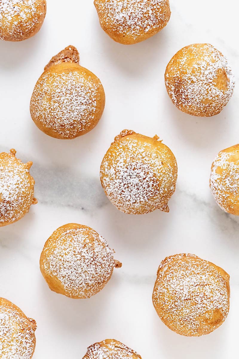 Powdered sugar dusted on fried cookie dough bites on a white marble counter.