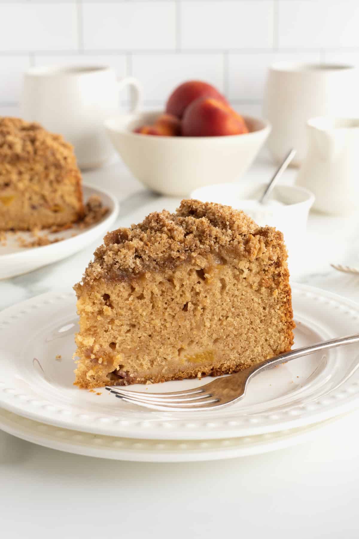A slice of peach coffee cake on a white plate with a fork.