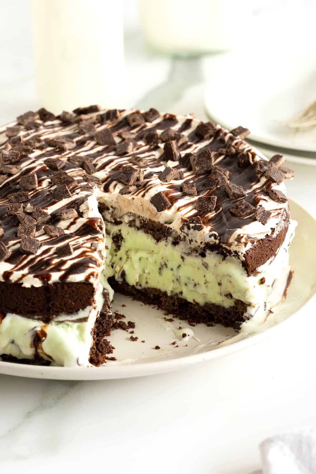 An ice cream cake with a chocolate cookie bottom and mint chocolate chip ice cream in the middle, covered in whipped topping, chocolate sauce and chopped Andes mints.