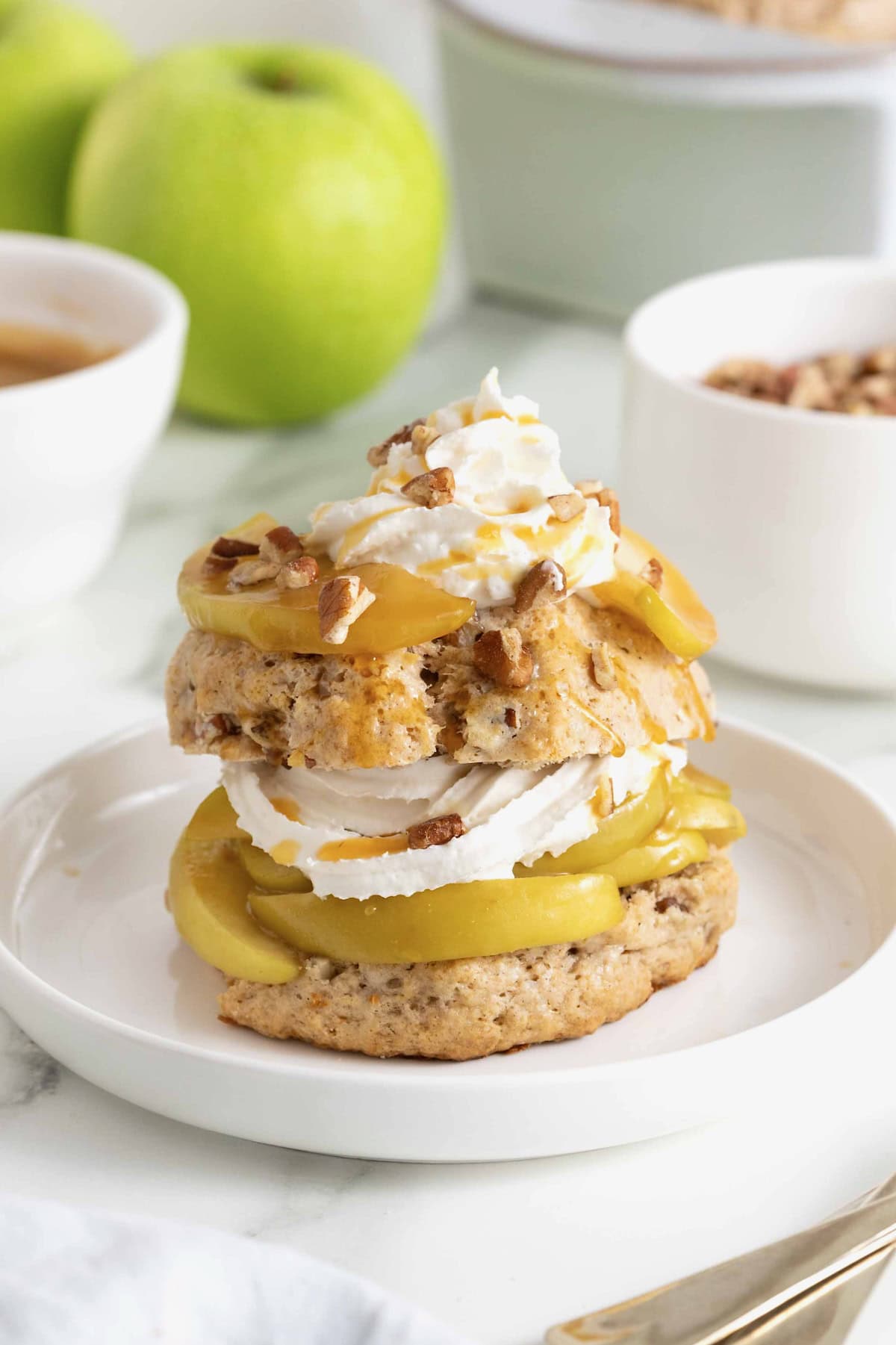A caramel apple pecan shortcake topped with whipped cream and garnished with pecan pieces on a white rimmed plate.