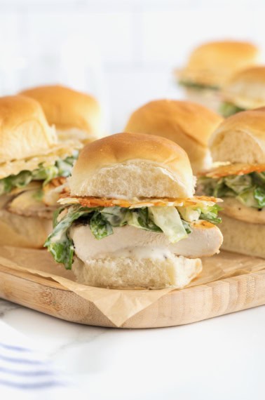 Six grilled chicken caesar sliders on a wooden cutting board.