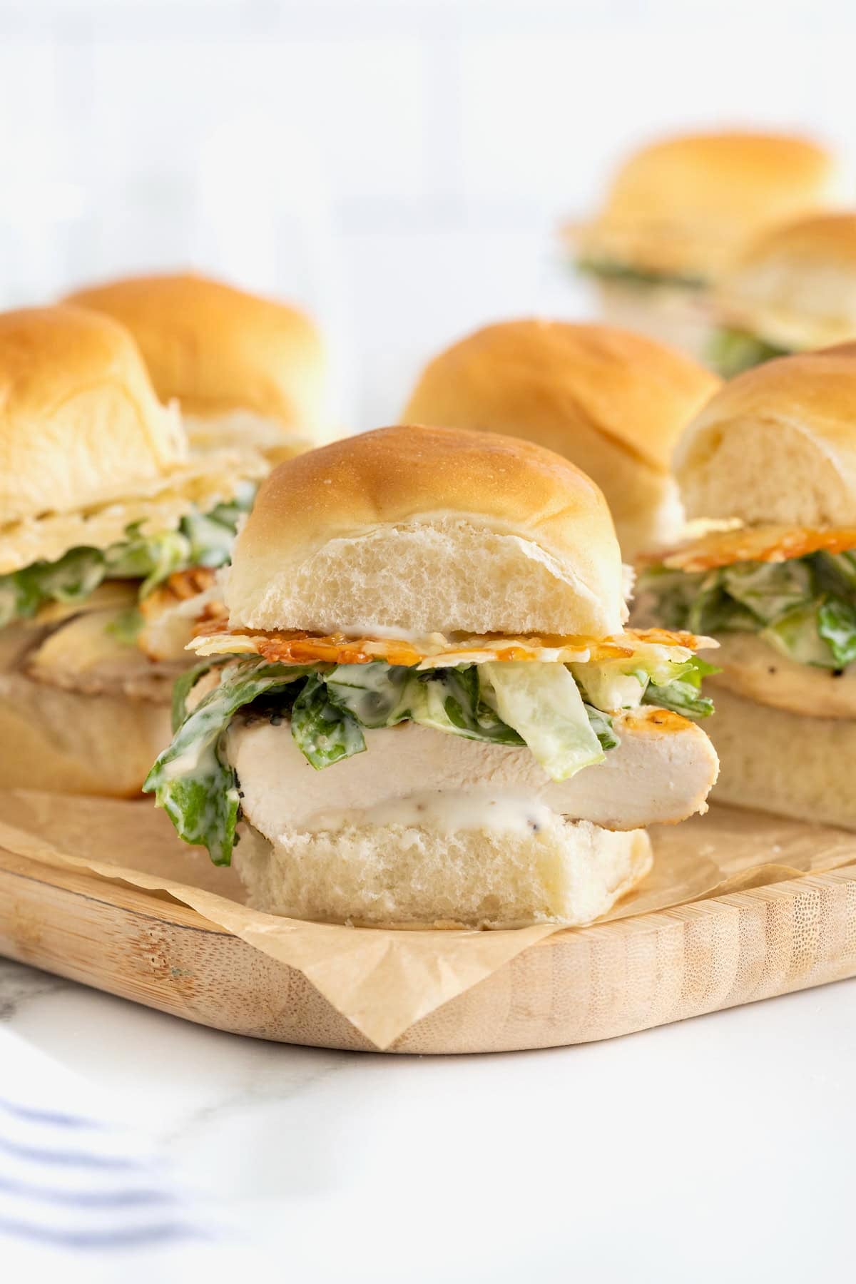 Six grilled chicken caesar sliders on a wooden cutting board.