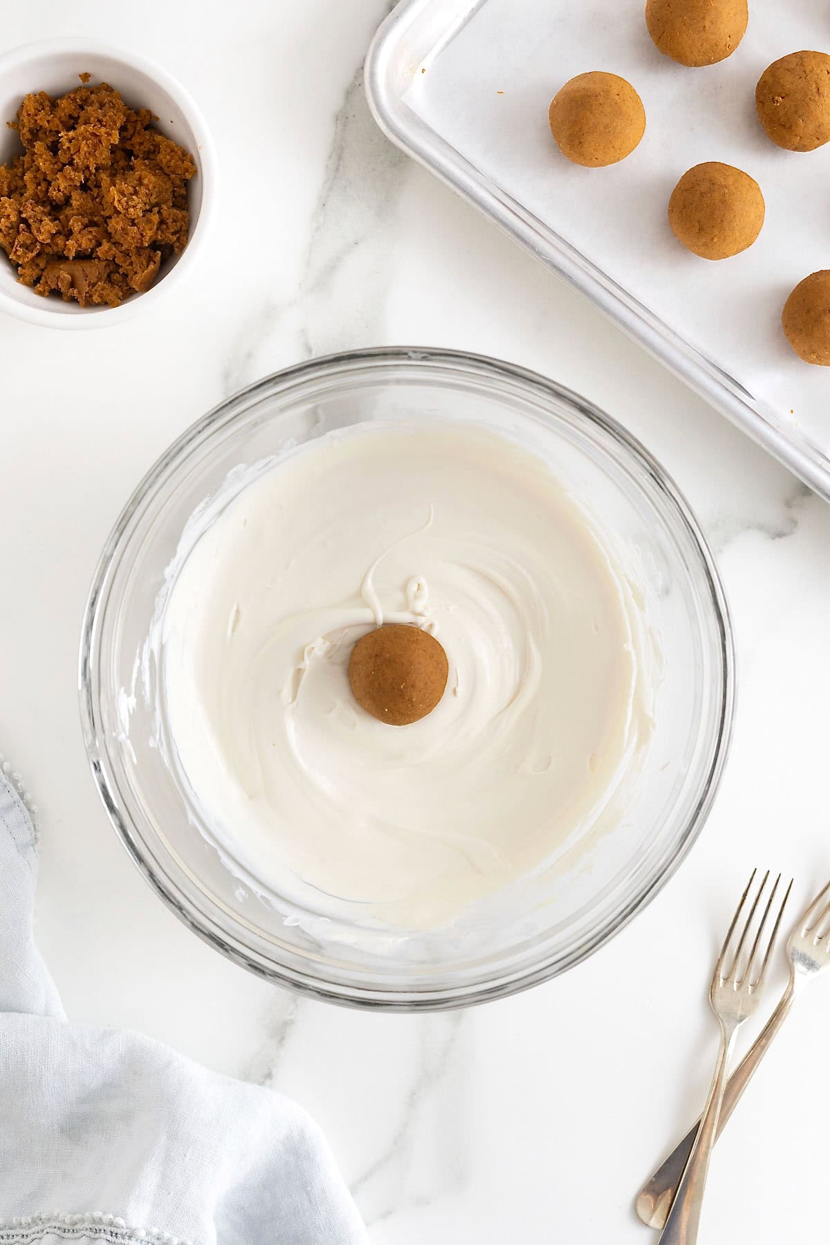 A pumpkin cake ball in a glass bowl of melted white candy coating.