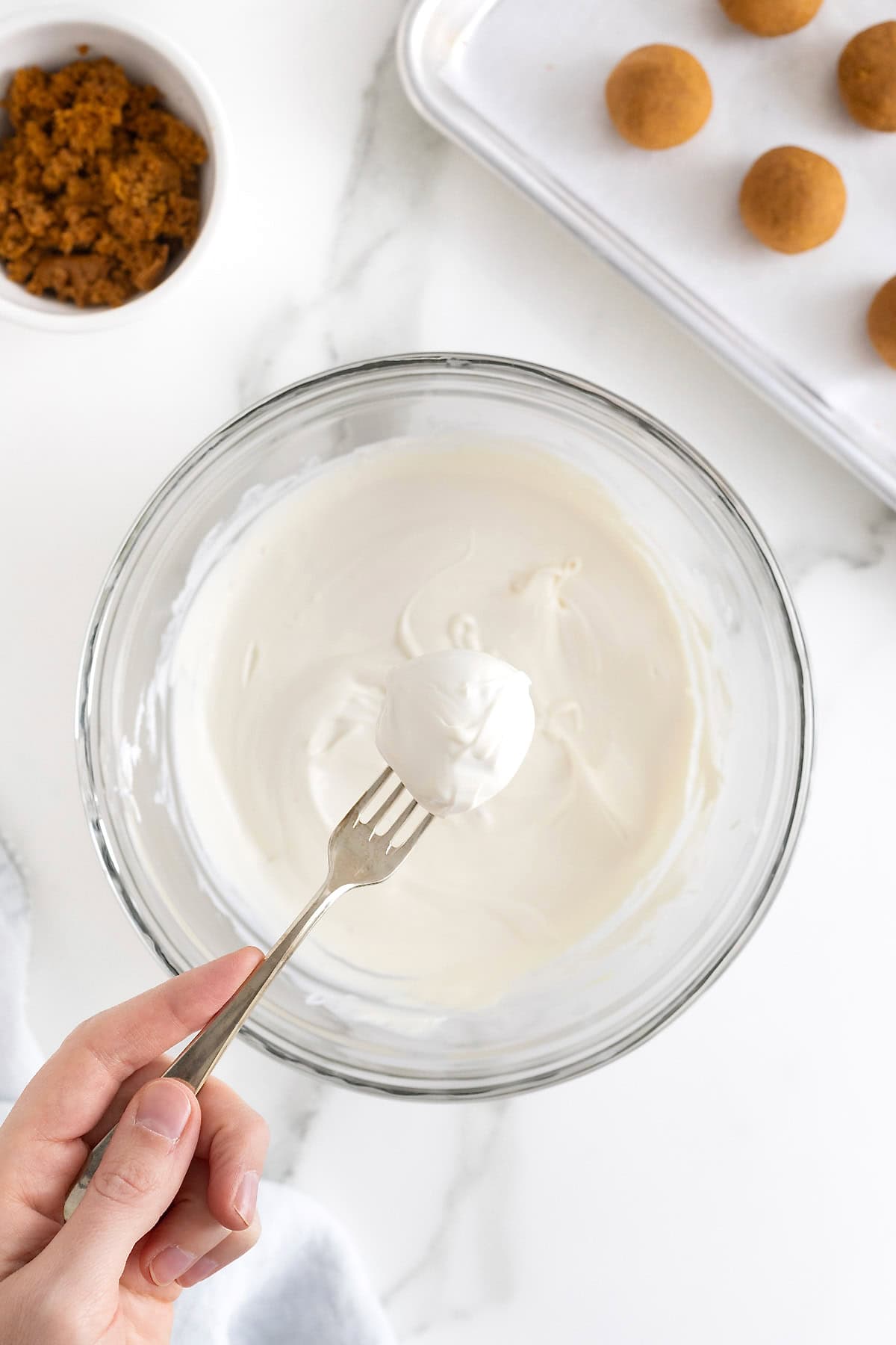 A cake ball on a fork over a glass bowl of white melted candy coating.