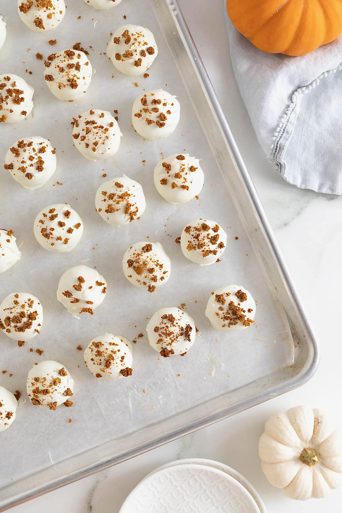 Pumpkin cake balls on a parchment-covered aluminum baking sheet.