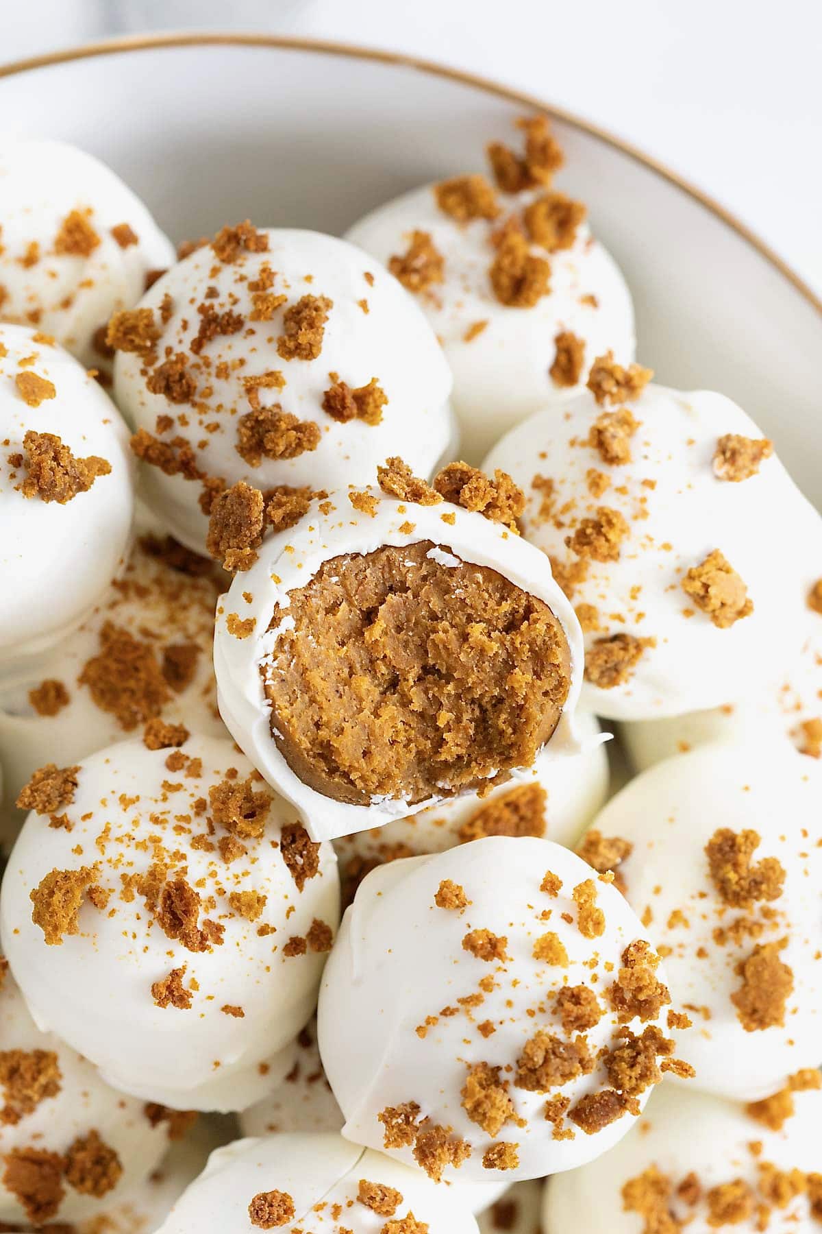 A large white gold-rimmed serving dish filled with pumpkin spice cake balls.