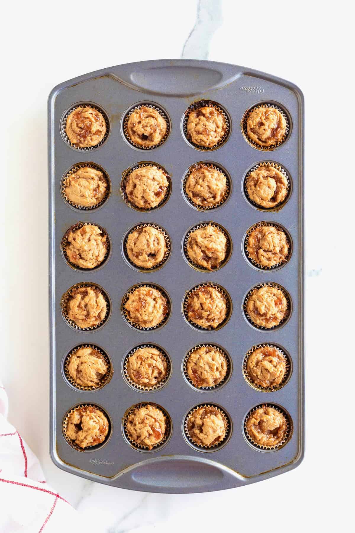 24 mini peanut butter and jelly muffins in an aluminum muffin pan.