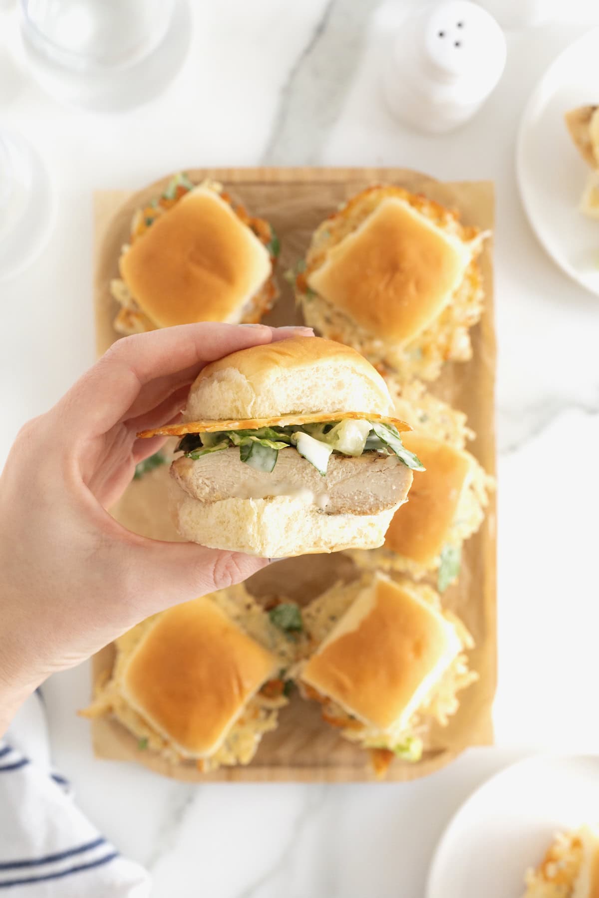 A hand holding a grilled chicken caesar slider.