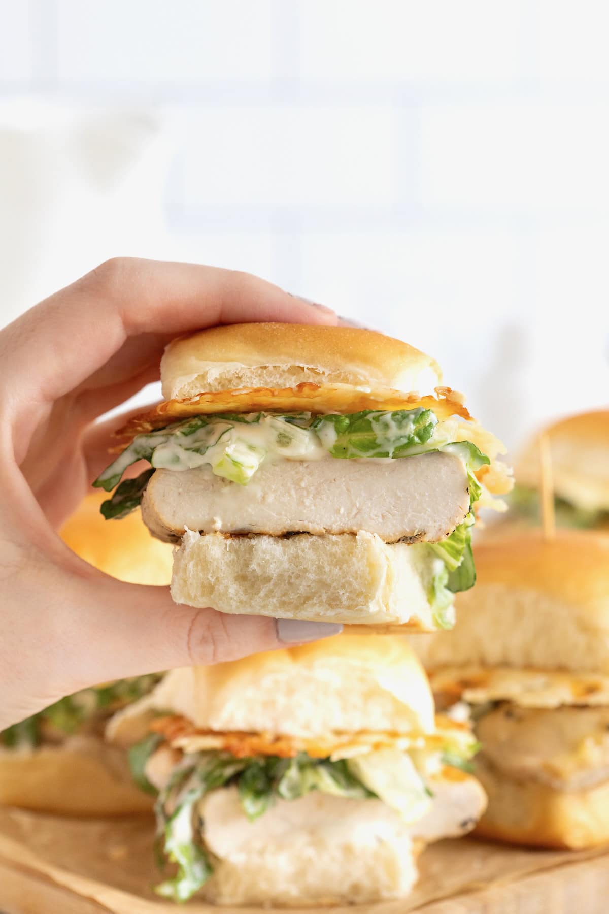 A hand holding a grilled chicken caesar slider.