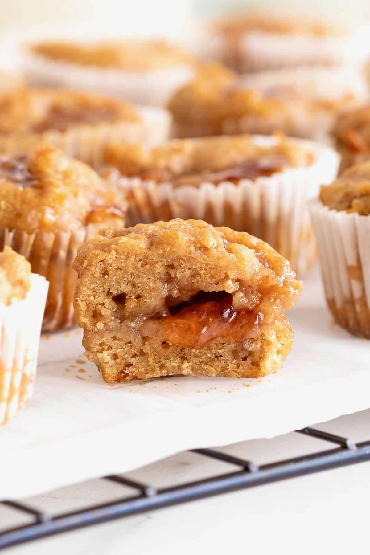 Peanut butter and jelly muffins on a parchment lined cooling rack. The front-most muffin is cut in half revealing the jelly center.