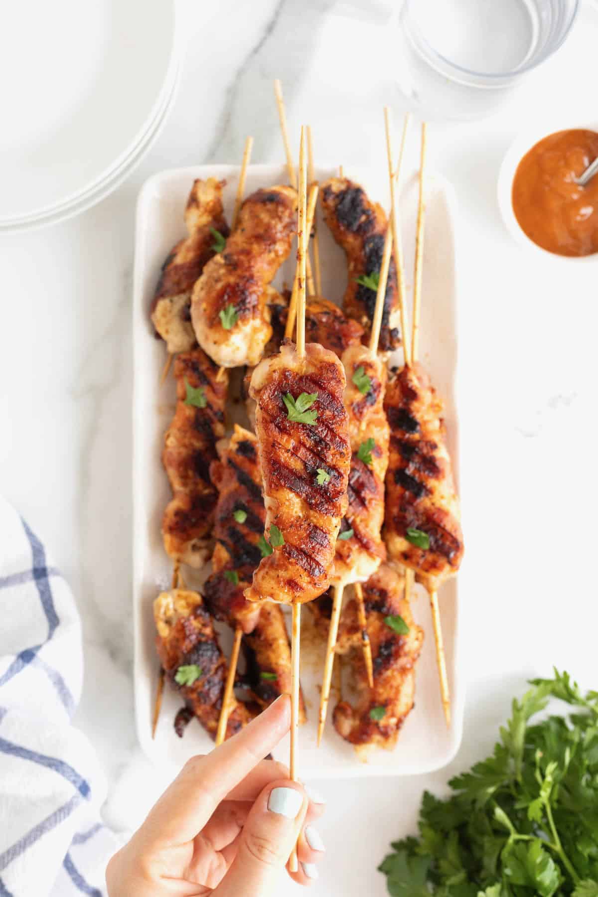 A rectangular white serving platter of grilled chicken on bamboo skewers.
