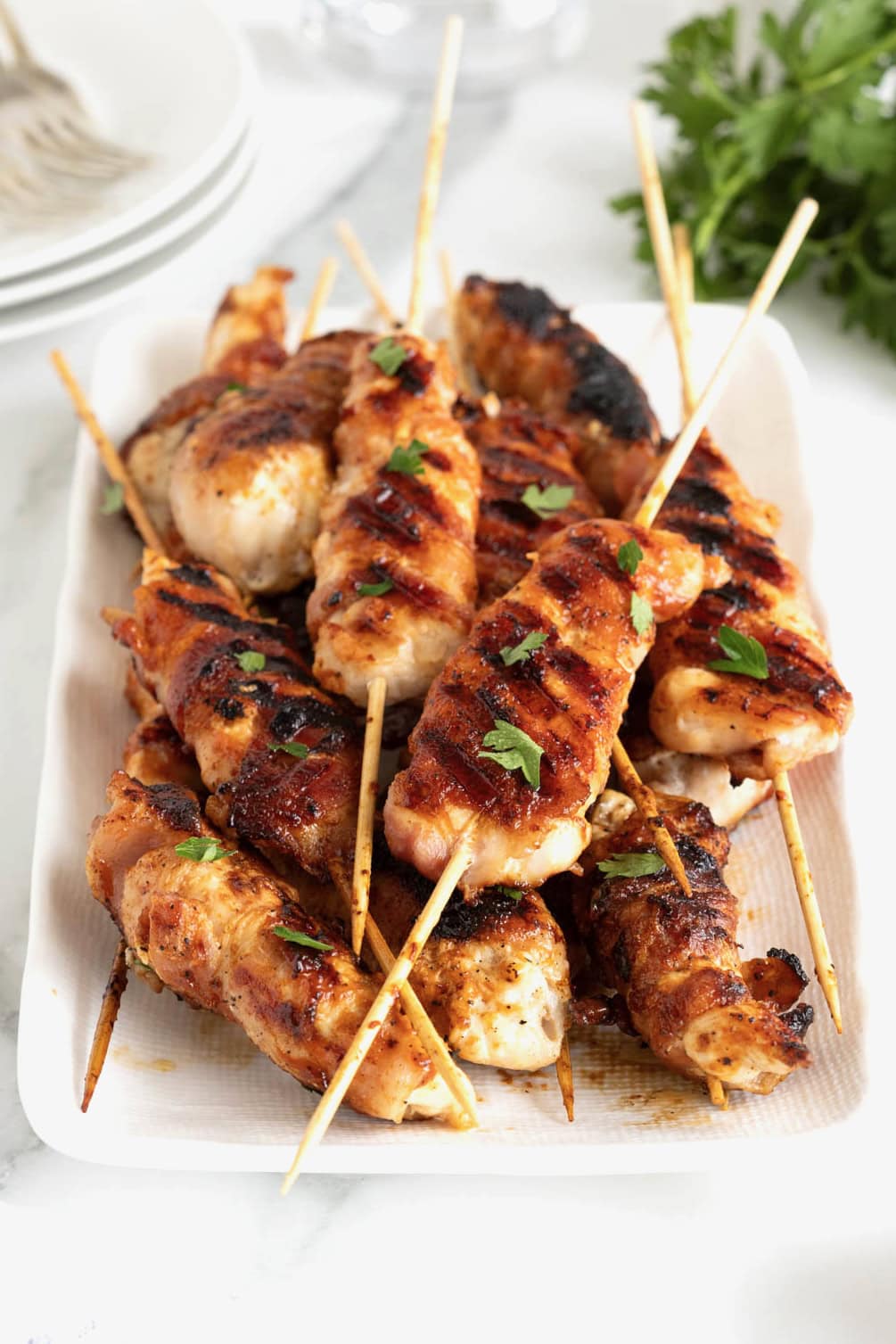 A rectangular white serving platter of grilled chicken on bamboo skewers.