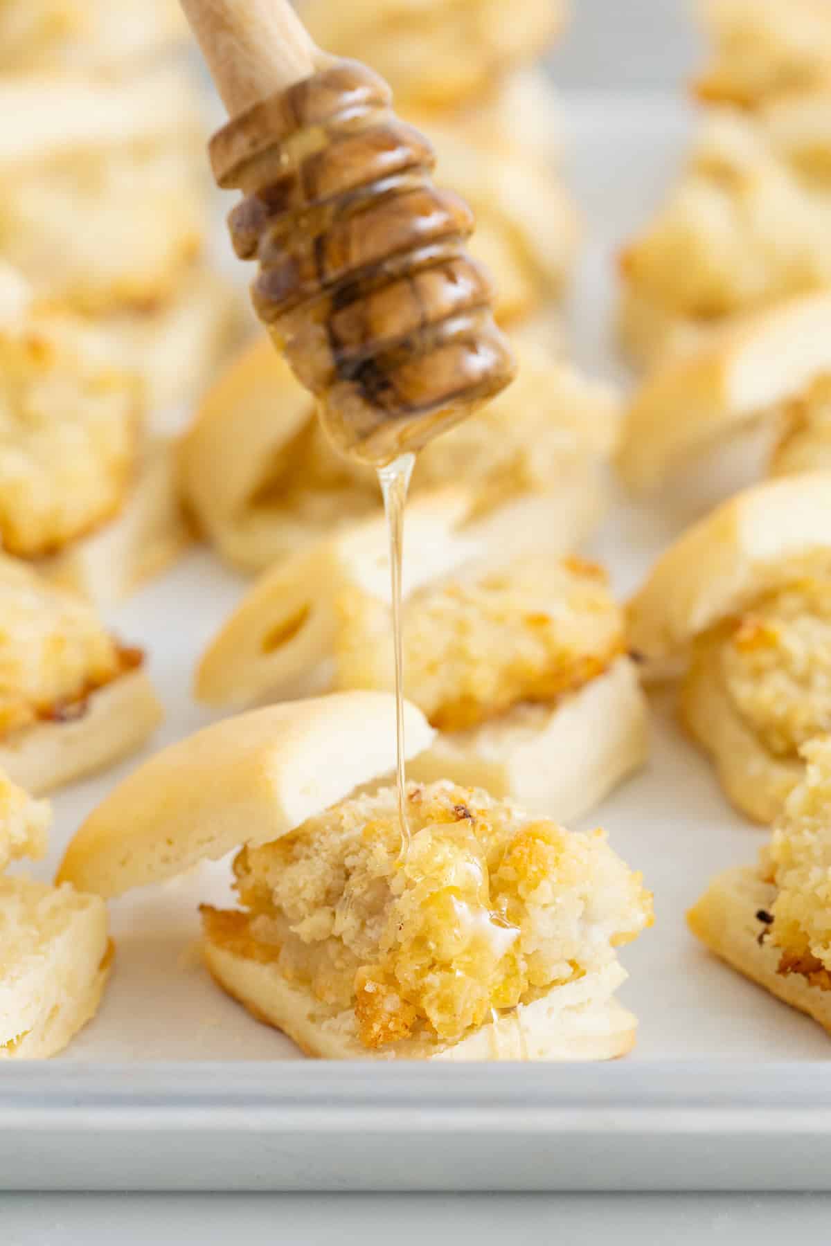 Honey being drizzled on a mini chicken biscuit.