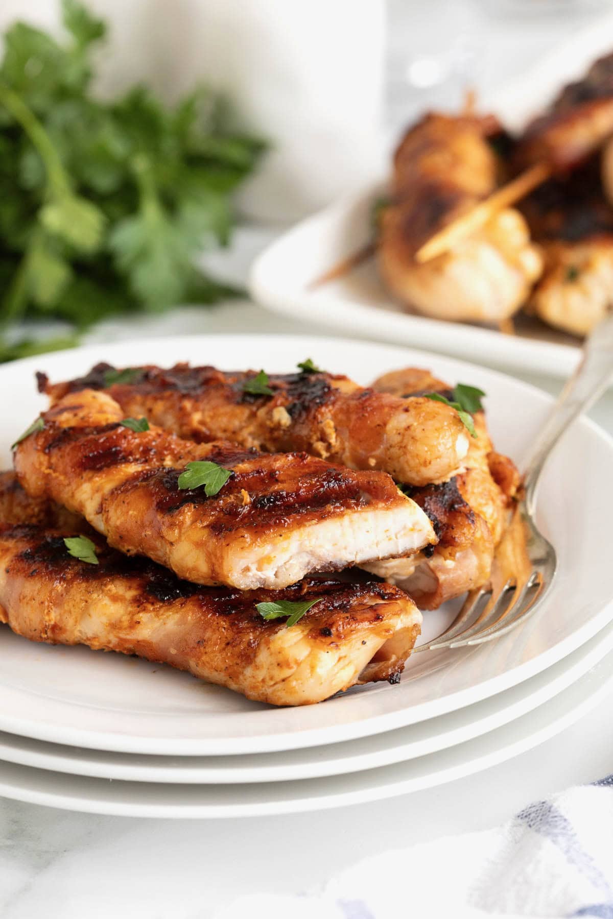 A small white plate piled with bacon wrapped chicken skewers.