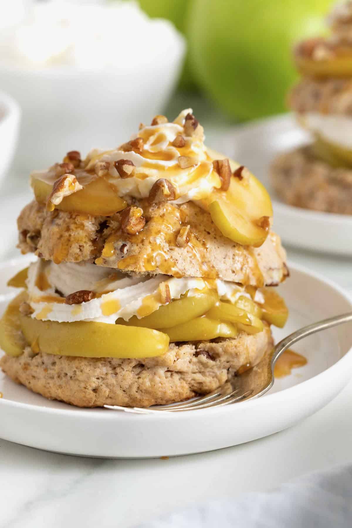 A caramel apple pecan shortcake topped with whipped cream and garnished with pecan pieces on a white rimmed plate.