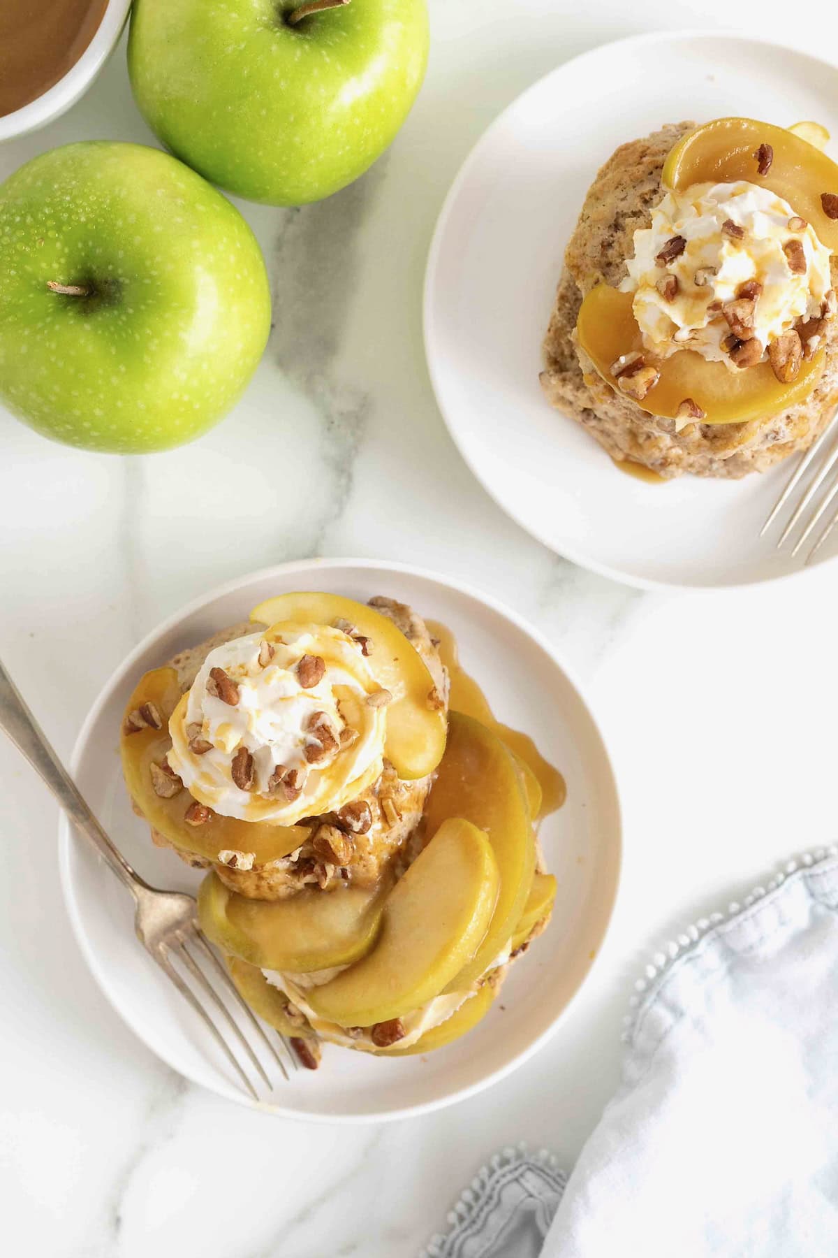 A caramel apple pecan shortcake topped with whipped cream and garnished with pecan pieces on a white rimmed plate.