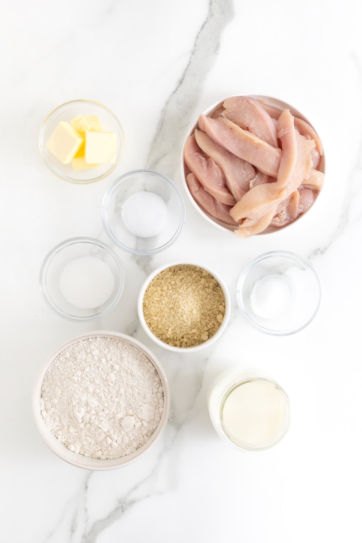 Ingredients to make mini chicken biscuits in small glass dishes on a white marble counter.