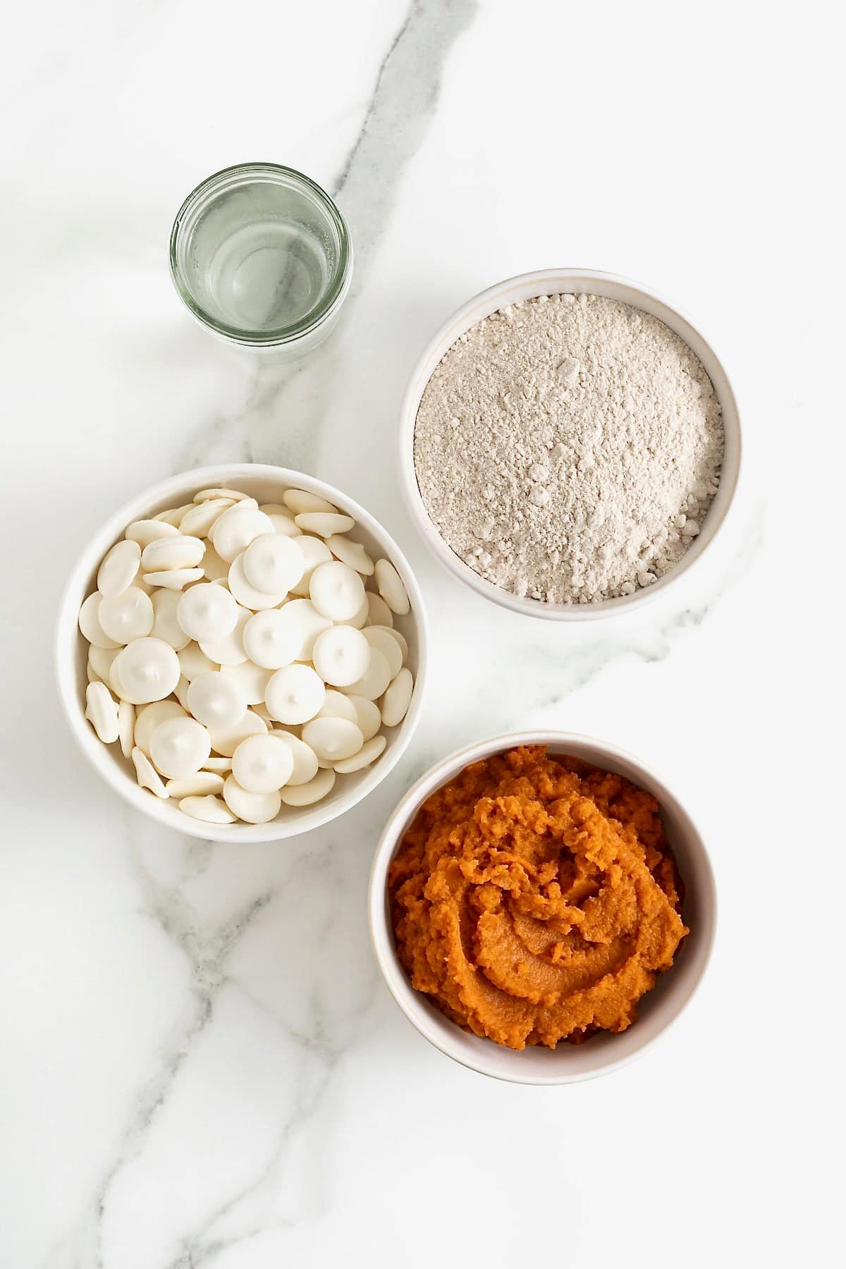 Ingredients to make pumpkin spice cake balls in white dishes on a white marble counter.