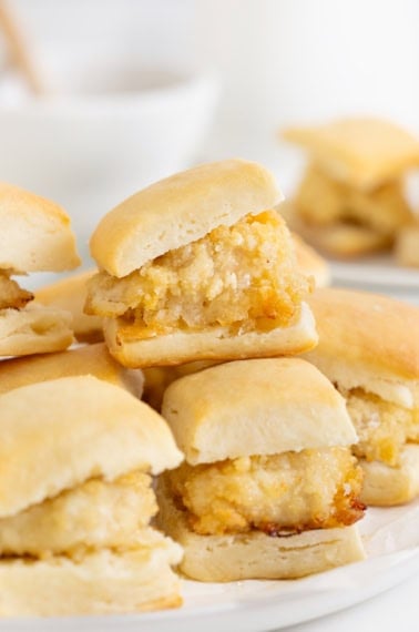 A pile of mini chicken biscuits that are drizzled with honey.