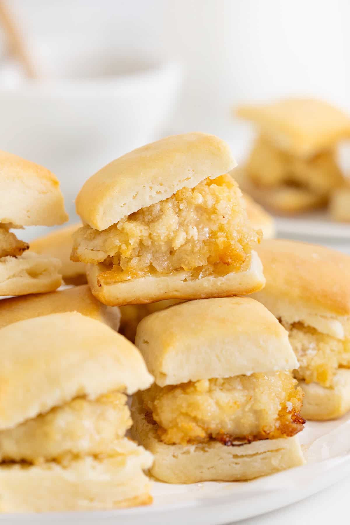 A pile of mini chicken biscuits that are drizzled with honey.
