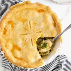 A broccoli and cheese pot pie with a serving taken out of it on a white marble counter.