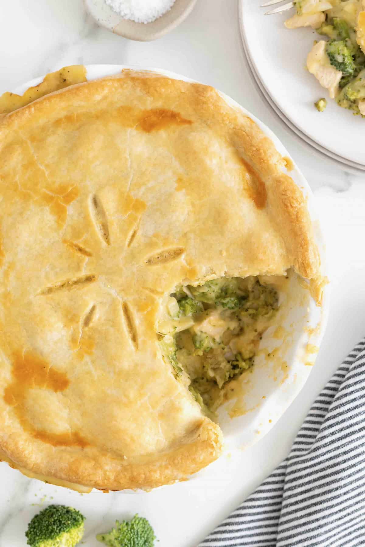 A broccoli and cheese pot pie with a serving taken out of it on a white marble counter.