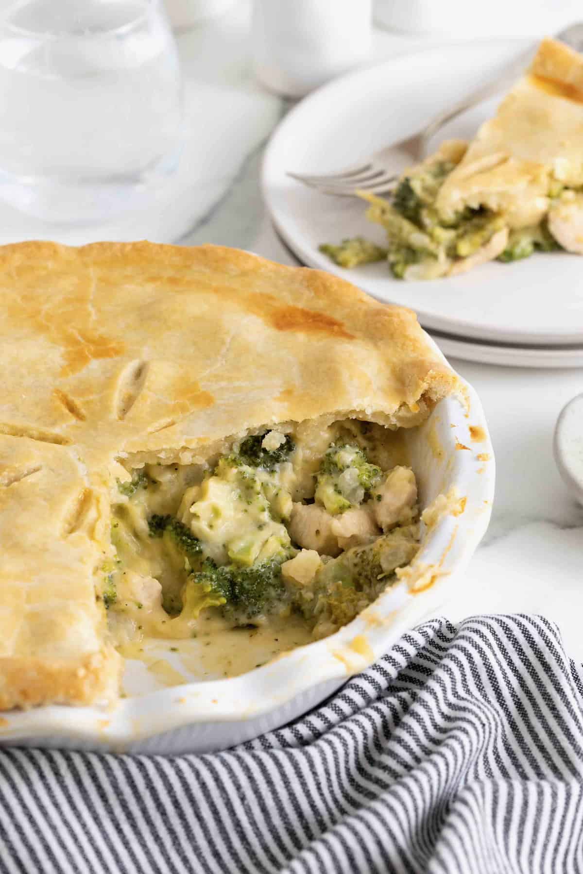 A broccoli and cheese pot pie with a serving taken out of it on a white marble counter.